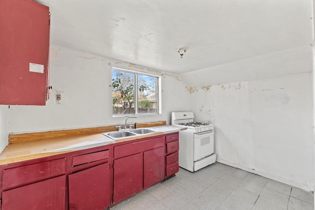 kitchen with white gas range oven, red cabinets, vaulted ceiling, light floors, and a sink