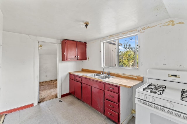 kitchen with white range with gas stovetop, red cabinets, vaulted ceiling, light countertops, and a sink