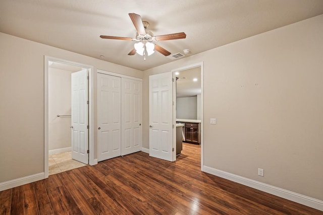 unfurnished bedroom featuring a closet, visible vents, dark wood-type flooring, ensuite bath, and baseboards