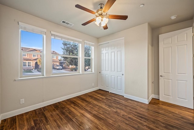 unfurnished bedroom with baseboards, multiple windows, visible vents, and dark wood-type flooring