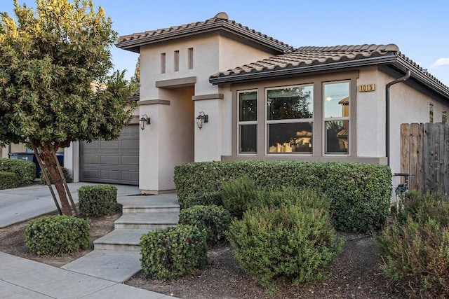 mediterranean / spanish house featuring driveway, a tiled roof, an attached garage, fence, and stucco siding