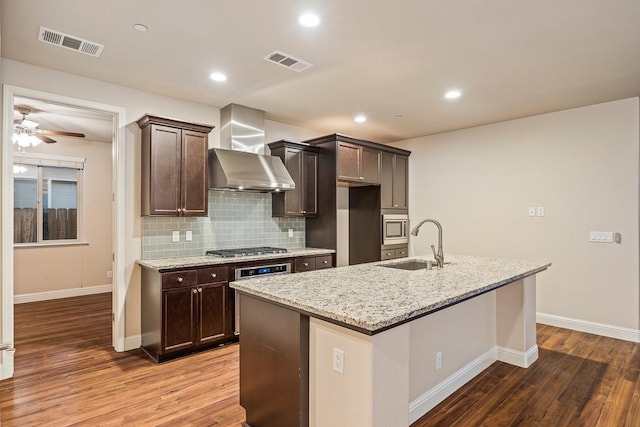 kitchen featuring wall chimney range hood, appliances with stainless steel finishes, a sink, and visible vents