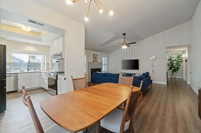 dining room with vaulted ceiling, a brick fireplace, wood finished floors, and visible vents