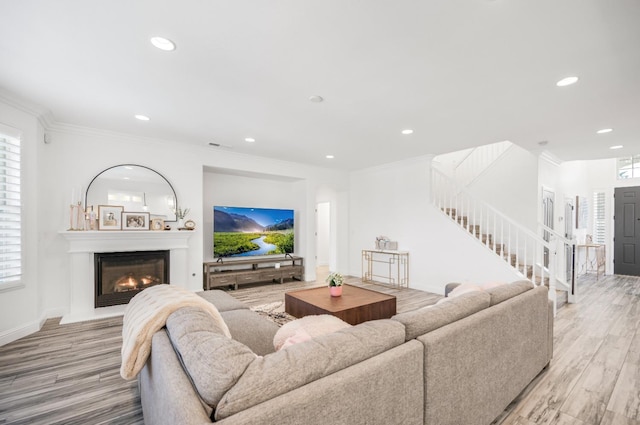 living room with recessed lighting, ornamental molding, stairway, light wood-type flooring, and a glass covered fireplace