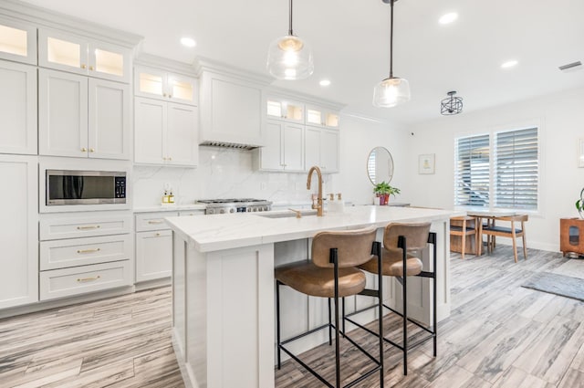 kitchen with a sink, a kitchen breakfast bar, custom exhaust hood, tasteful backsplash, and stainless steel microwave