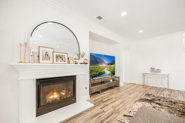 living area with wood finished floors, visible vents, baseboards, ornamental molding, and a glass covered fireplace