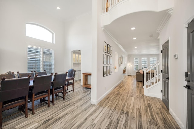 entrance foyer featuring arched walkways, baseboards, stairs, light wood-style floors, and ornamental molding