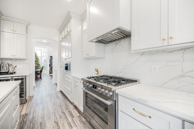 kitchen featuring arched walkways, stainless steel stove, premium range hood, white cabinets, and ornamental molding