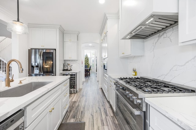 kitchen with arched walkways, custom exhaust hood, stainless steel appliances, white cabinets, and a sink