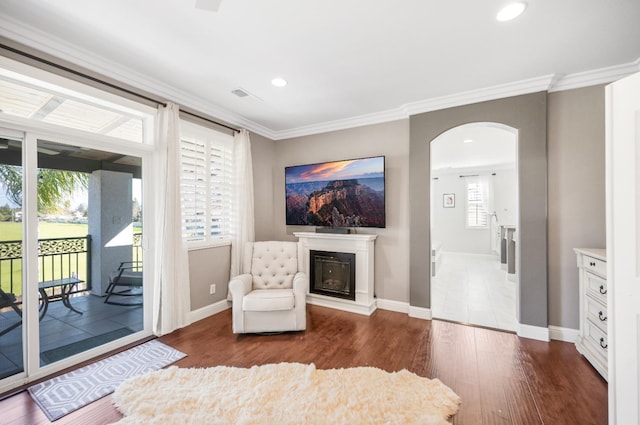 living area featuring arched walkways, ornamental molding, dark wood-type flooring, a glass covered fireplace, and baseboards