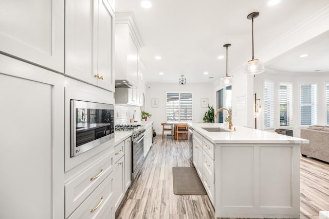 kitchen with stainless steel appliances, a sink, white cabinetry, open floor plan, and ornamental molding