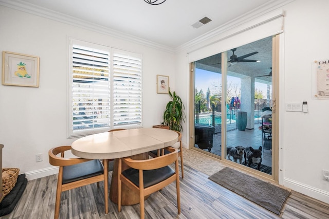 dining space featuring visible vents, ornamental molding, a ceiling fan, wood finished floors, and baseboards