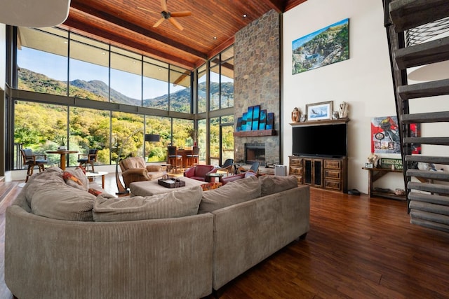 living room featuring wood ceiling, a high ceiling, wood finished floors, and a stone fireplace