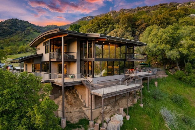 back of house at dusk featuring a mountain view and a balcony