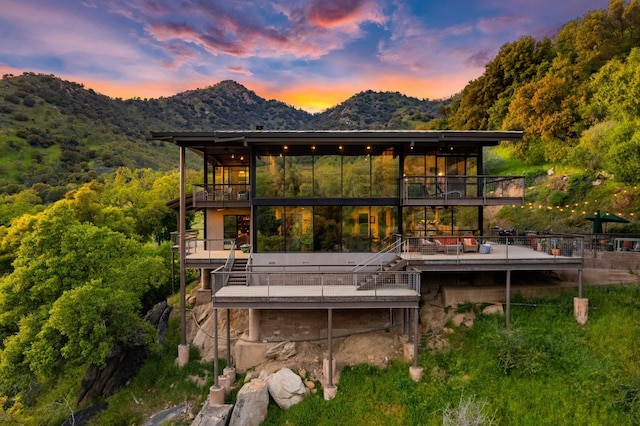 back of house at dusk featuring a balcony and a mountain view