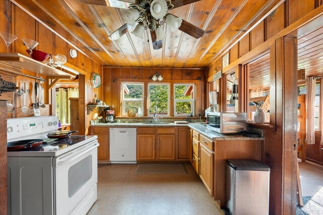 kitchen featuring wooden ceiling, wooden walls, white appliances, a sink, and a ceiling fan