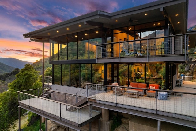 back of house at dusk with a mountain view, an outdoor living space, and a balcony