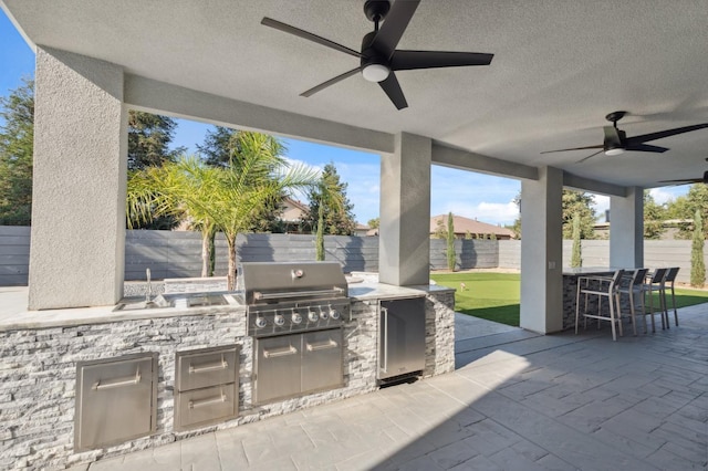 view of patio / terrace featuring a fenced backyard, a grill, a ceiling fan, exterior kitchen, and outdoor dining space