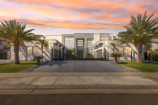 contemporary house with stone siding, driveway, a gate, and stucco siding