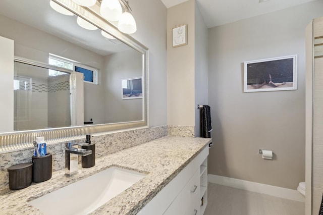 bathroom with toilet, a stall shower, baseboards, and vanity