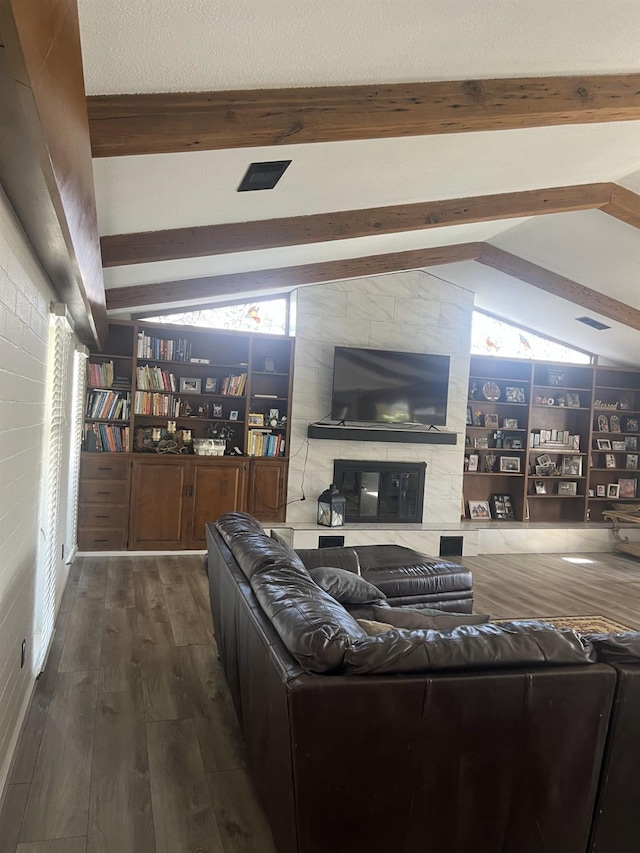 living area featuring lofted ceiling with beams, a large fireplace, a textured ceiling, and wood finished floors