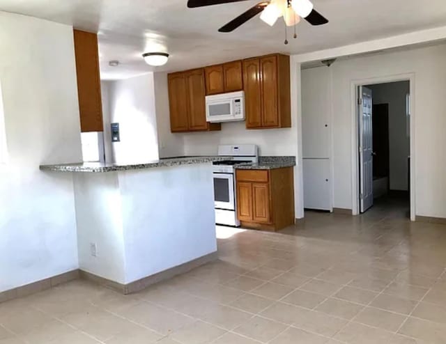 kitchen featuring white microwave, brown cabinetry, stainless steel gas stove, dark stone countertops, and baseboards