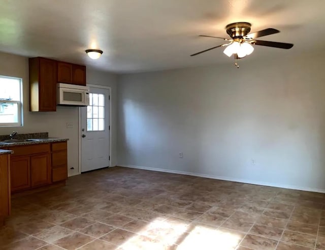 kitchen with baseboards, dark countertops, white microwave, brown cabinets, and a sink