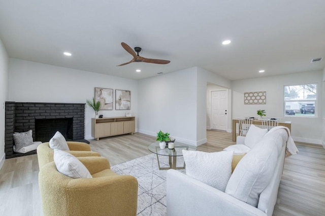 living room featuring visible vents, baseboards, light wood-type flooring, a fireplace, and recessed lighting