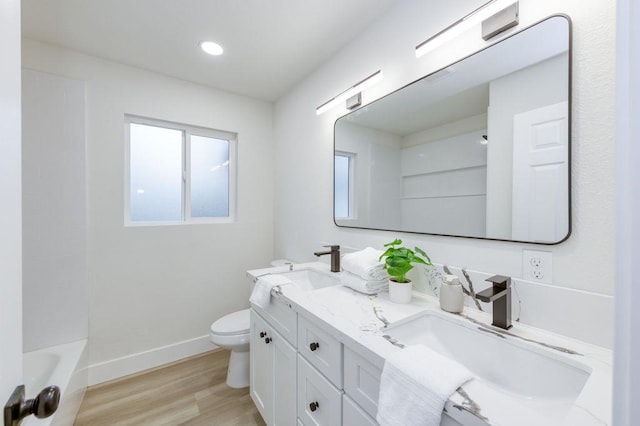 full bath featuring double vanity, baseboards, toilet, wood finished floors, and a sink