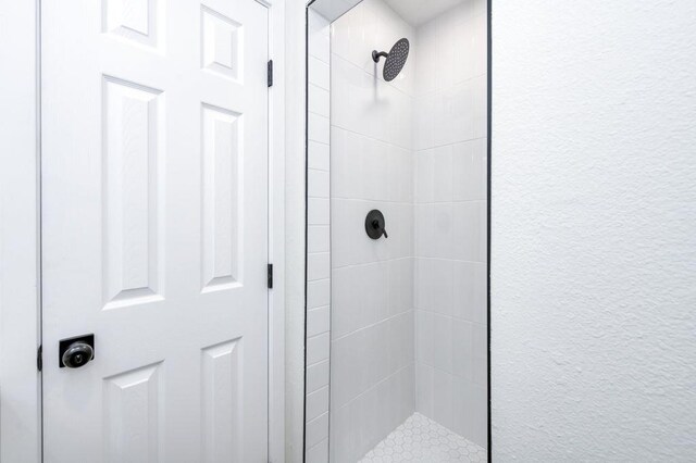 full bath featuring tiled shower and a textured wall