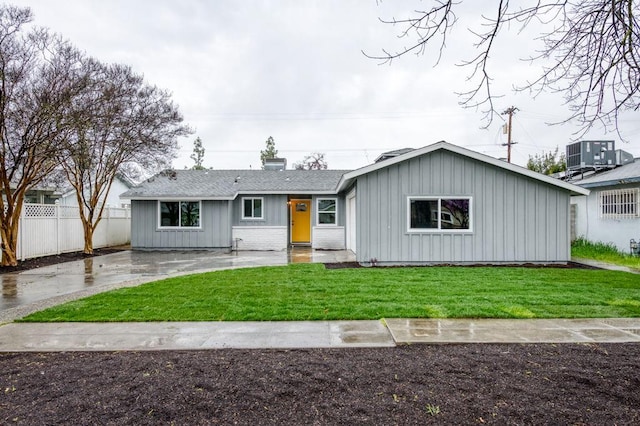 ranch-style home with cooling unit, a shingled roof, fence, board and batten siding, and a front yard