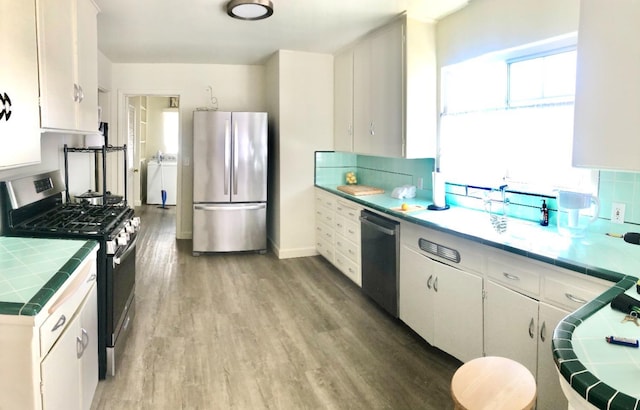 kitchen with washer / clothes dryer, tile counters, light wood-style floors, appliances with stainless steel finishes, and backsplash