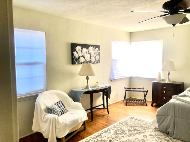 bedroom with ceiling fan, wood finished floors, baseboards, and a textured ceiling