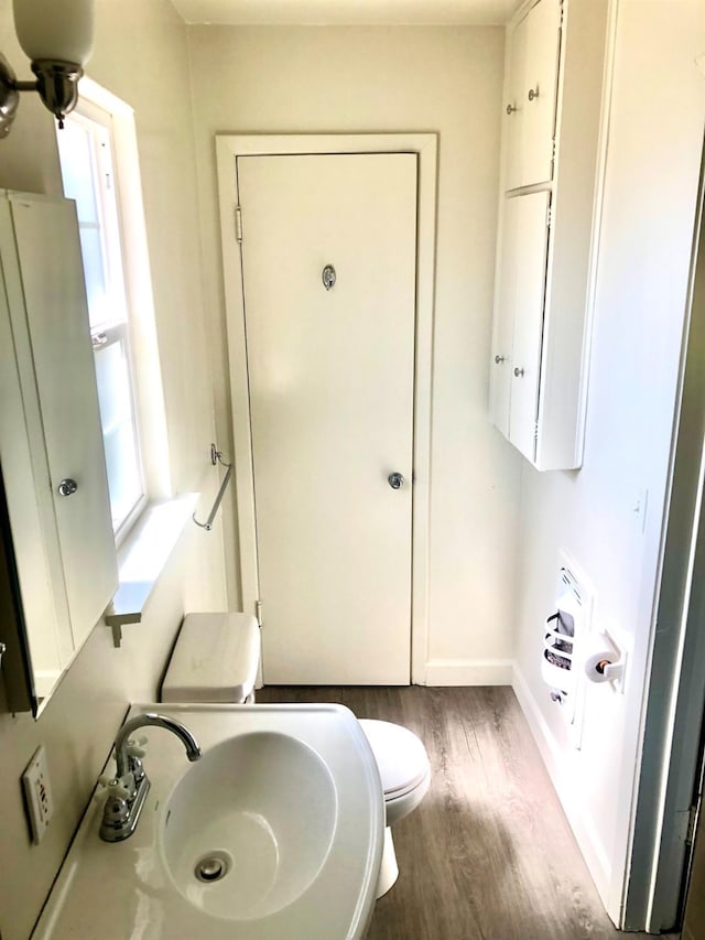 bathroom featuring toilet, wood finished floors, baseboards, and a sink