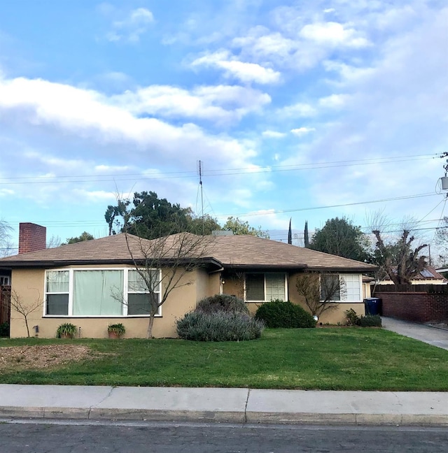 single story home featuring a front lawn, a chimney, driveway, and stucco siding