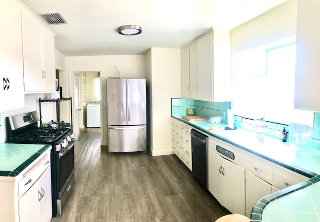 kitchen featuring tile countertops, visible vents, dark wood finished floors, washer / dryer, and stainless steel appliances