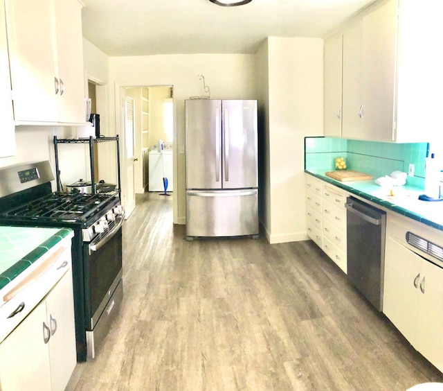 kitchen with tile countertops, washer / clothes dryer, light wood-style floors, appliances with stainless steel finishes, and white cabinetry