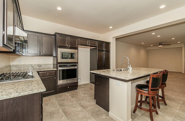 kitchen with appliances with stainless steel finishes, a sink, light stone countertops, under cabinet range hood, and a kitchen bar