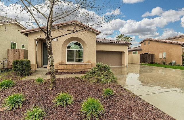 mediterranean / spanish house featuring concrete driveway, fence, a tile roof, and stucco siding