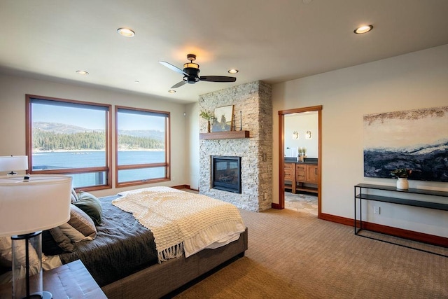 bedroom with recessed lighting, light colored carpet, a water view, a stone fireplace, and baseboards