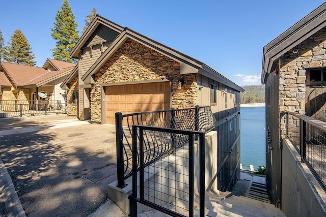 view of side of home featuring a garage, stone siding, a water view, and concrete driveway