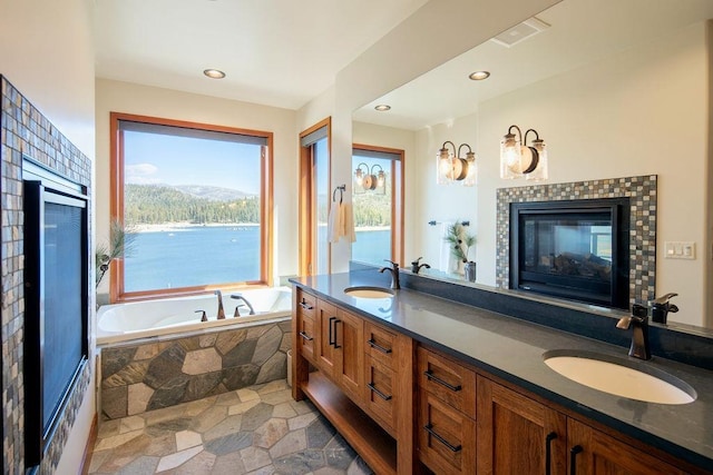 bathroom featuring stone finish floor, double vanity, a sink, and a bath