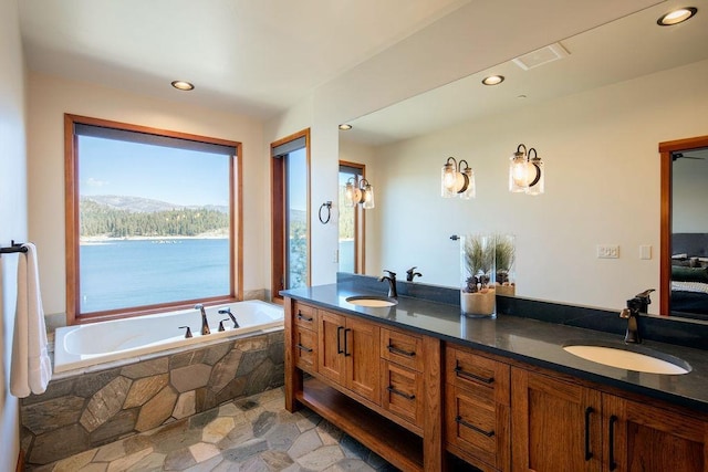 bathroom with double vanity, a sink, a bath, and stone tile floors