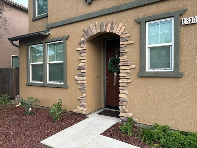 view of exterior entry with fence and stucco siding