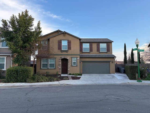 traditional-style home with a garage, concrete driveway, fence, and stucco siding