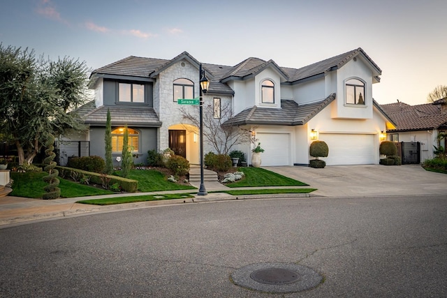 french provincial home with a tile roof, driveway, an attached garage, and stucco siding