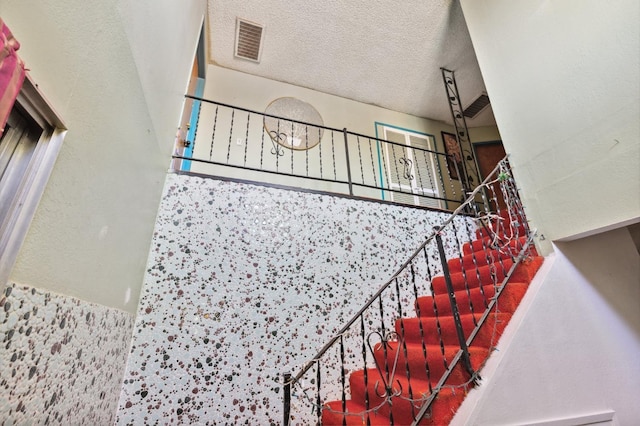 staircase with a textured ceiling, a textured wall, and visible vents