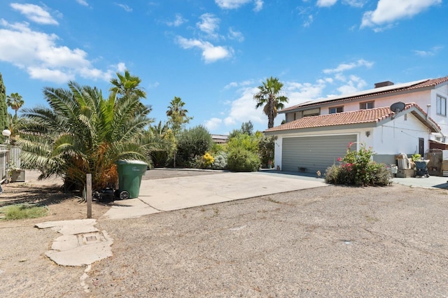 exterior space featuring driveway, a garage, a tile roof, roof mounted solar panels, and stucco siding