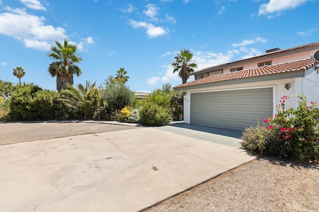 view of side of property featuring a garage, a tiled roof, concrete driveway, and stucco siding