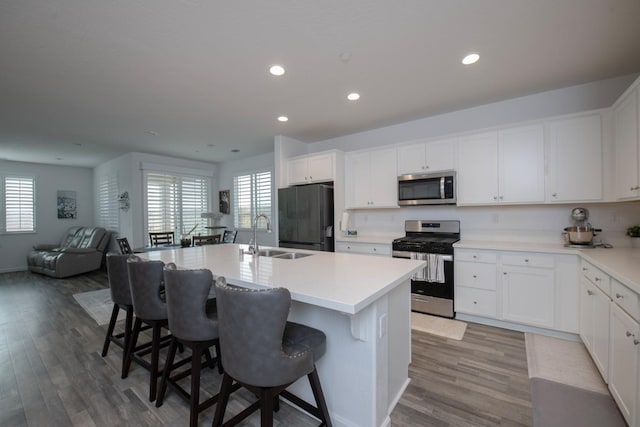 kitchen with stainless steel appliances, open floor plan, a kitchen island with sink, a sink, and wood finished floors